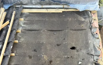 Deteriorated roofing membrane with a visible hole beneath removed tiles