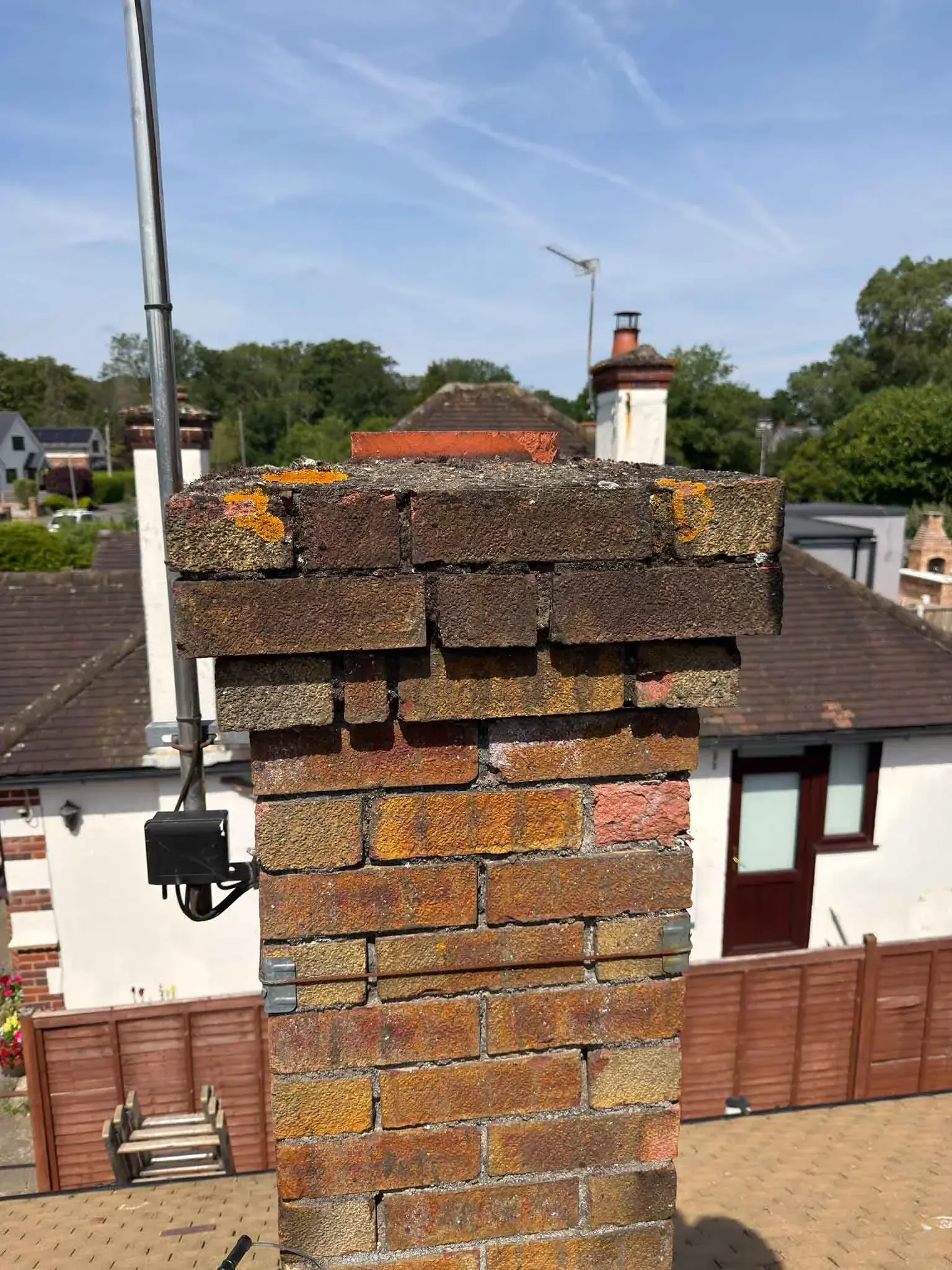 Chimney stack with a lichen-covered cap and weathered brickwork on a roof in Harrow, Greater London