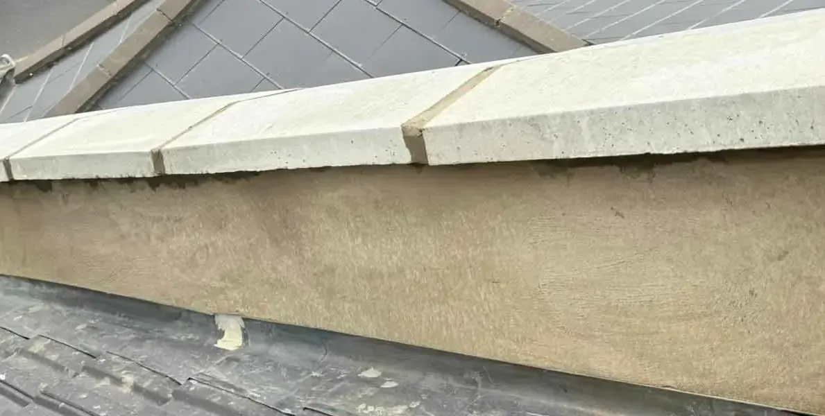 Rendered parapet wall topped with pale capstones beside a slate roof in Morden, Greater London