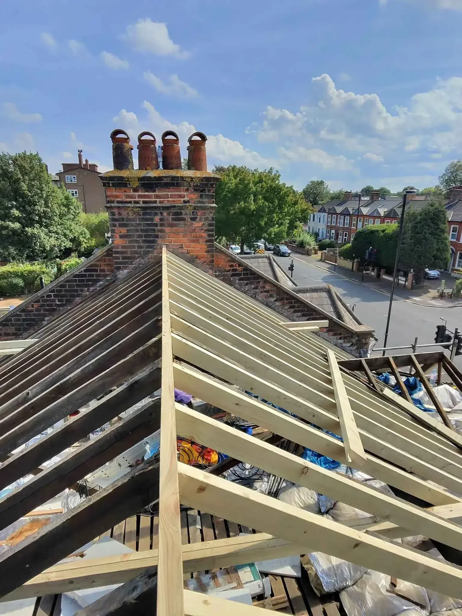 Exposed roof timbers during a full roof replacement in Hither Green, Greater London, with a chimney stack at the ridge