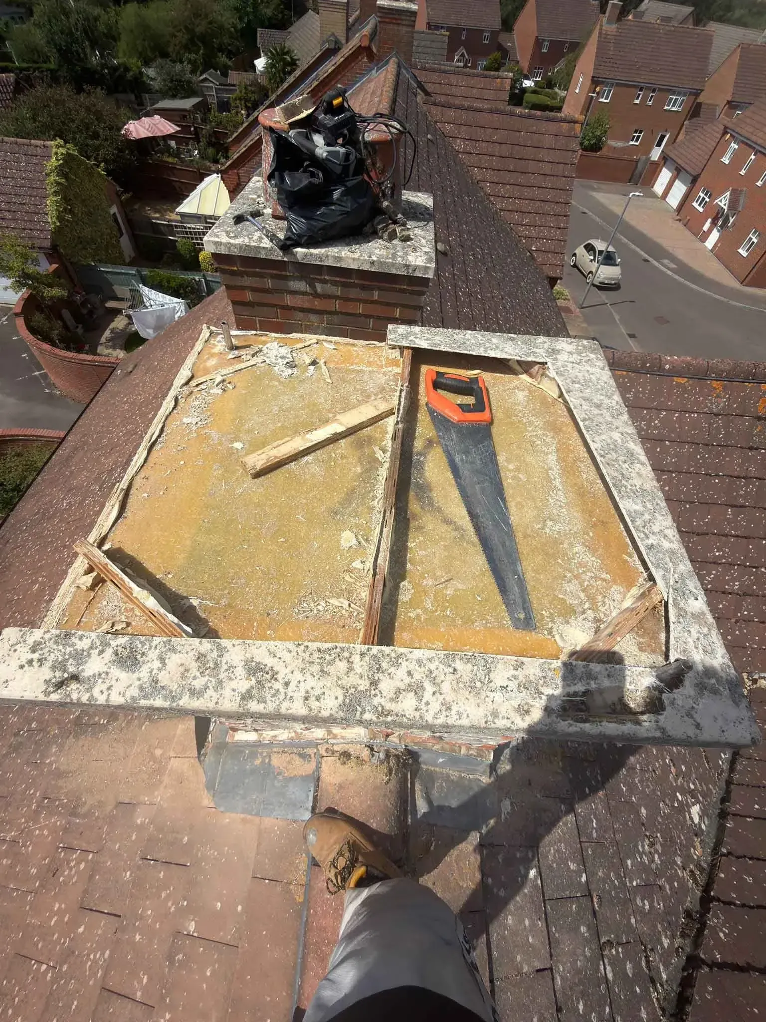 Open top of an artificial chimney on a tiled roof in Ascot, Berkshire, with a hand saw and cut timber resting on it