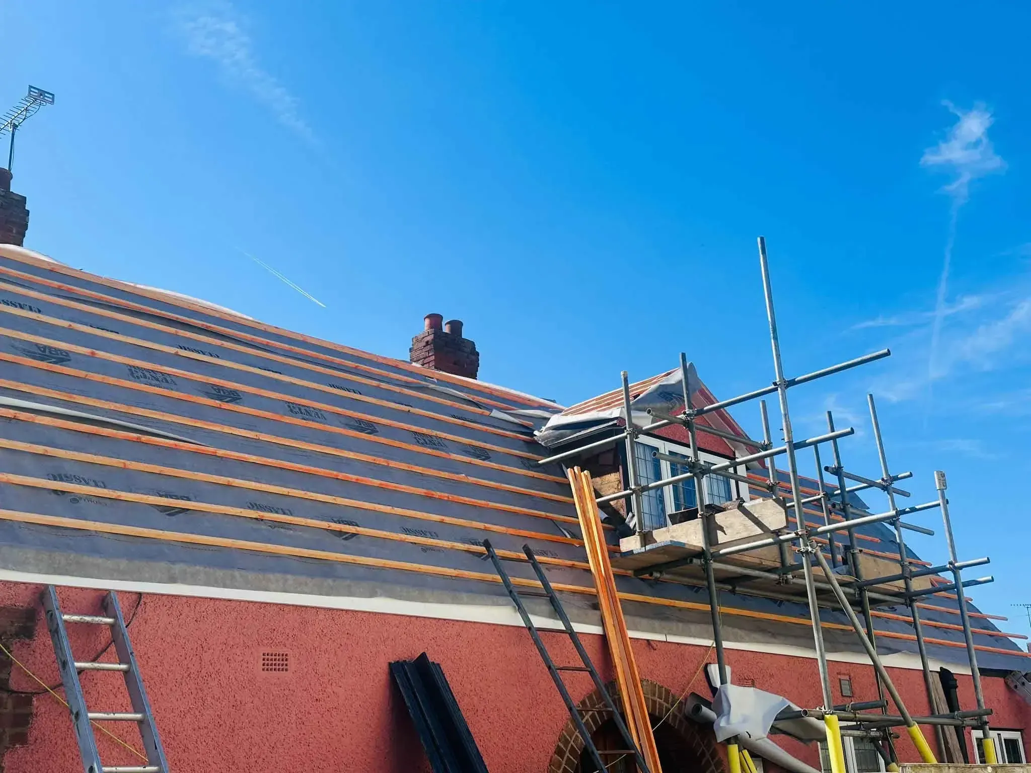 Battens fixed across a roof slope over the roofing membrane on a house in Bracknell, Berkshire, with scaffolding beside a dormer
