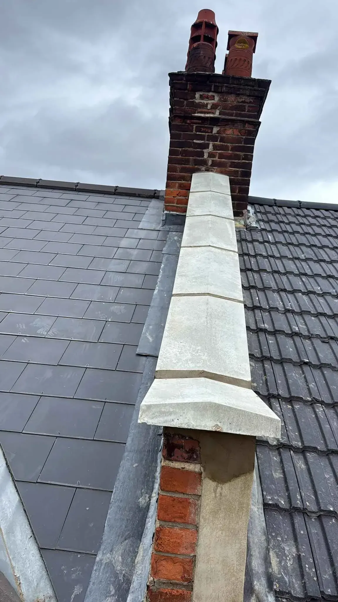 Capstone running up to a brick chimney with lead flashing beside the wall on a roof in Morden, Greater London