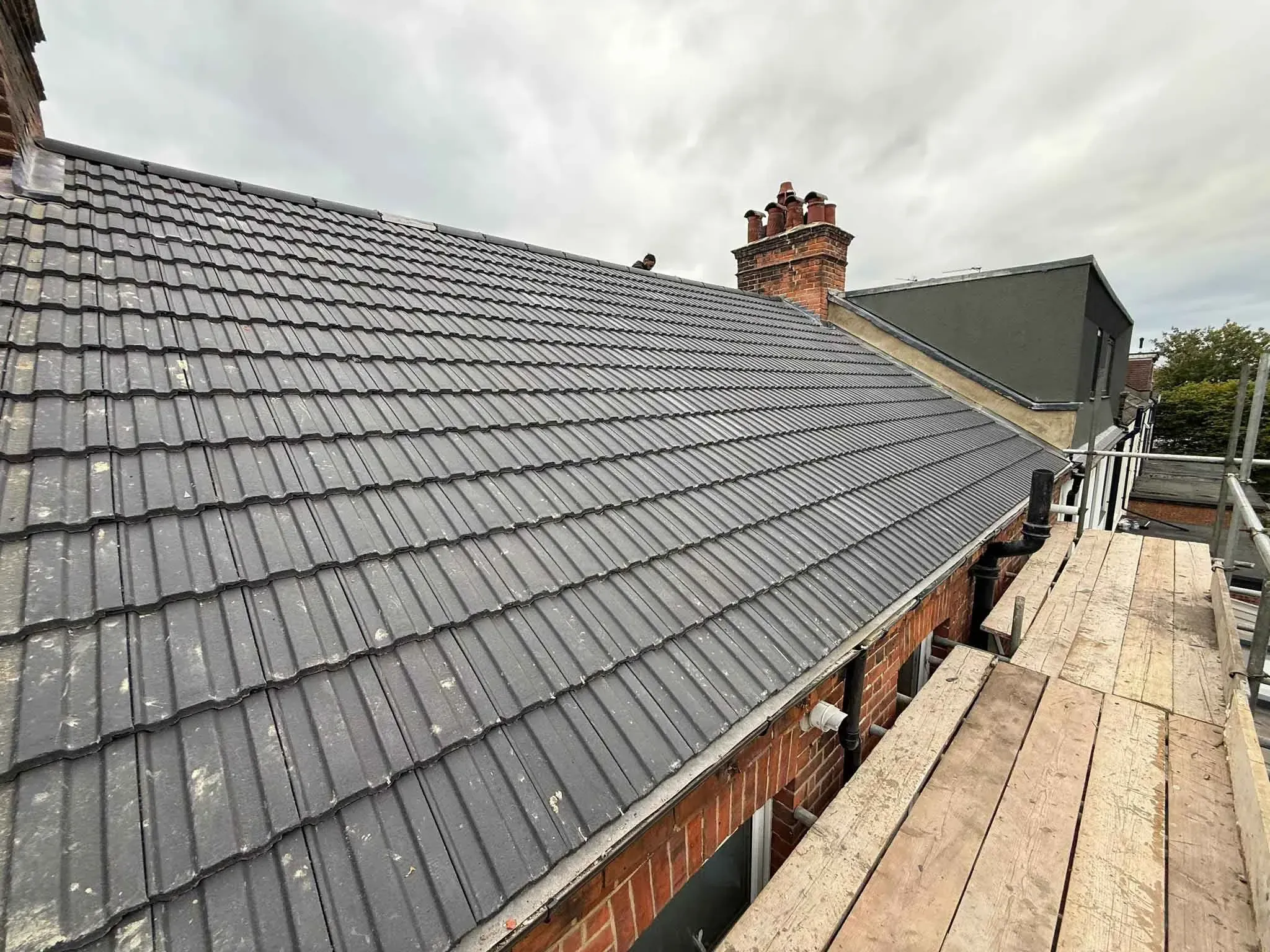 Long slope of charcoal-grey roof tiles in Hither Green, Greater London, with scaffold boards alongside