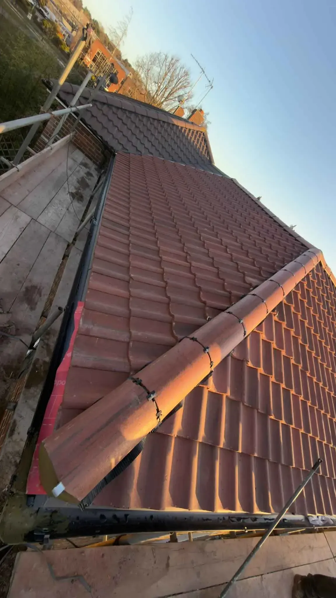 Dry ridge finishing at the edge of a newly tiled roof in Wokingham, Berkshire, with scaffold boards alongside