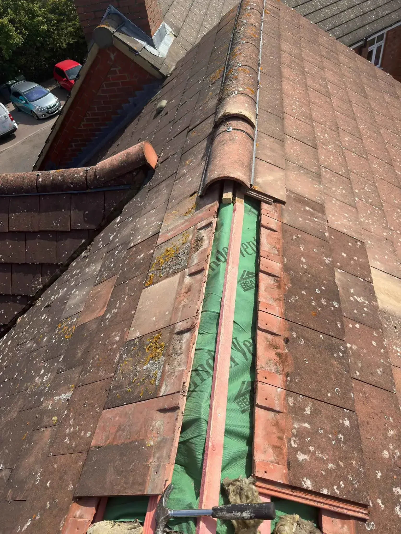 Strip of green membrane and battens beside a roof ridge in Ascot, Berkshire, with tiles in place on either side