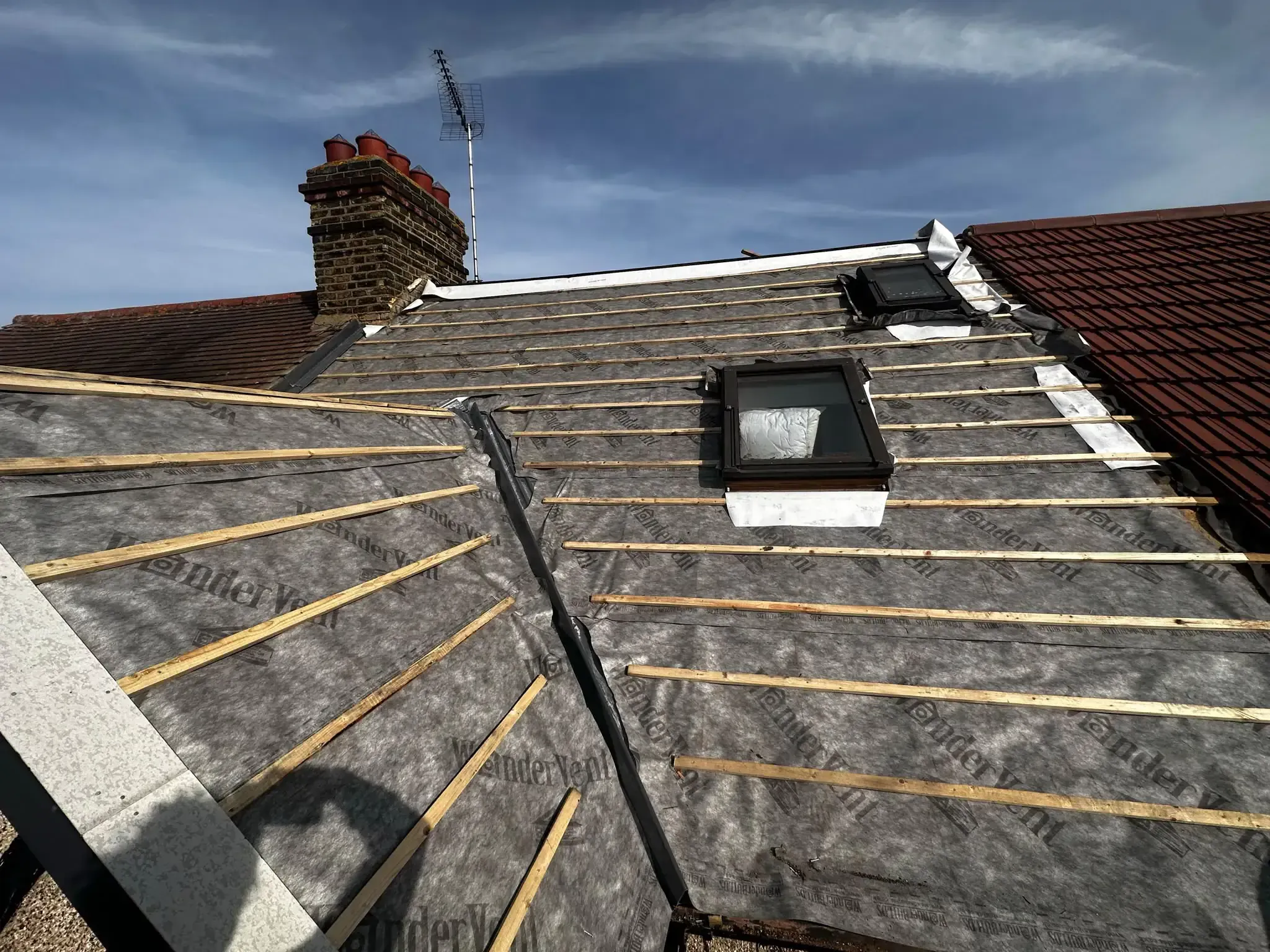 Membrane and battens exposed across connected roof slopes around two rooflights in Cobham