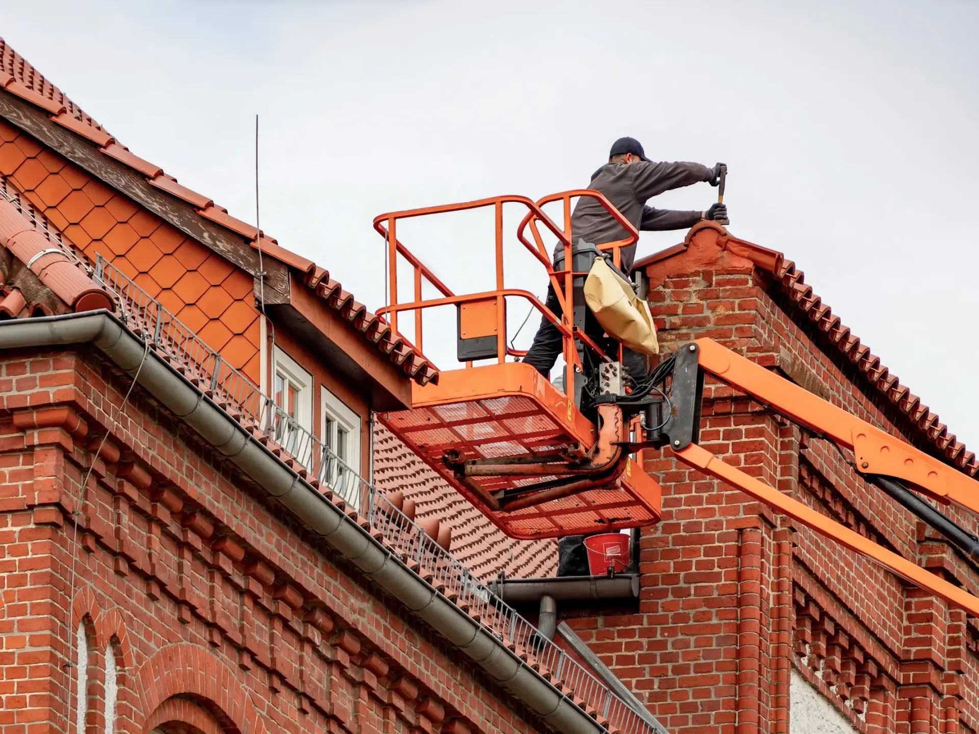 A roofer working from a raised platform beside a large tiled roof