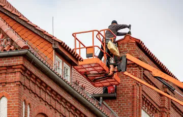 A roofer working from a platform beside a large tiled building