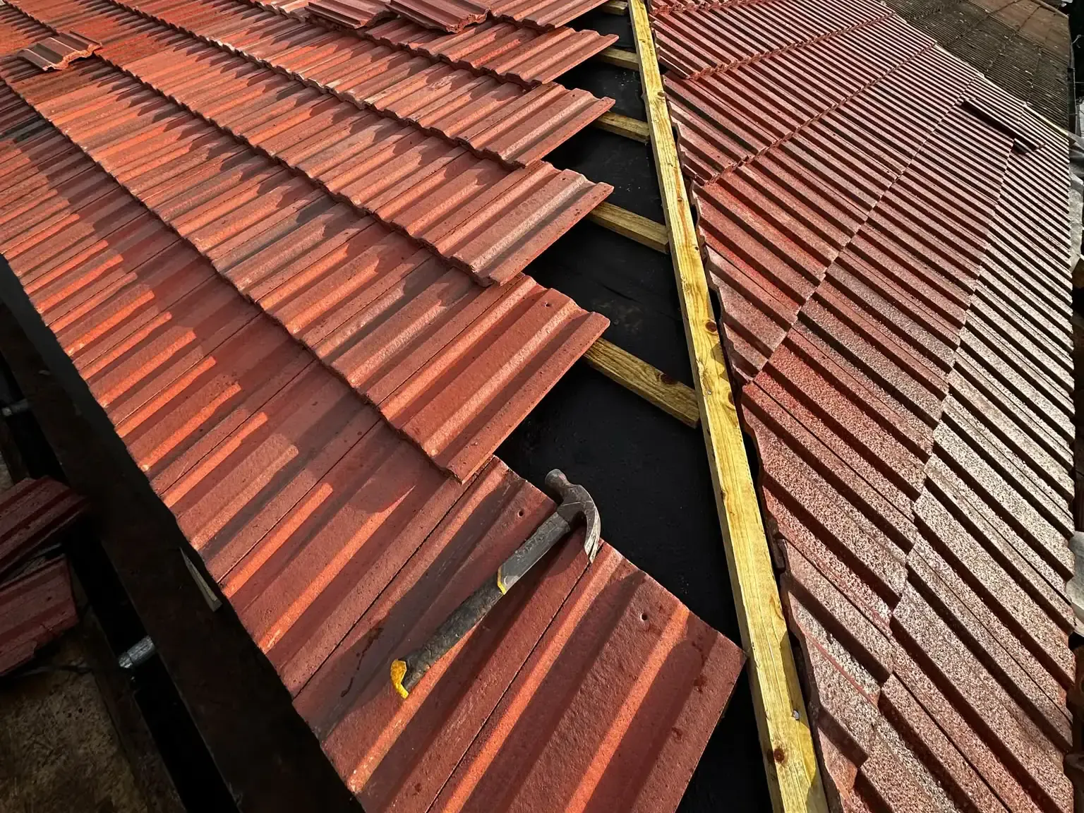 Red profiled roof tiles being installed over visible membrane and battens in Dorking