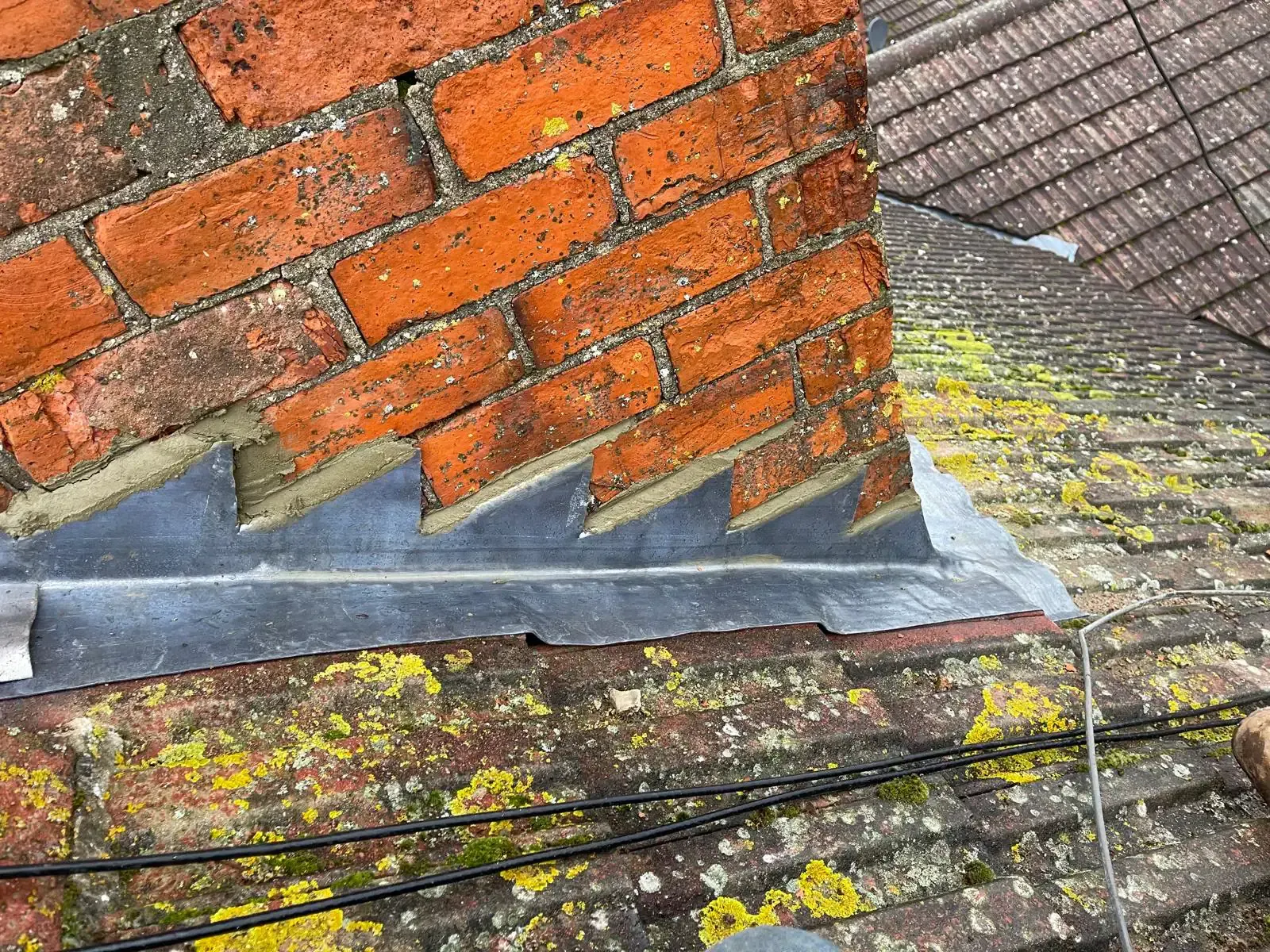 New lead step flashing installed along a brick chimney and tiled roof junction in Epsom