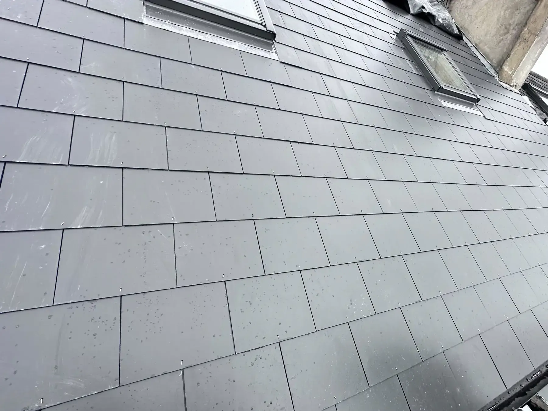 Grey tiled roof covering around roof windows and abutments during a documented project in Weybridge