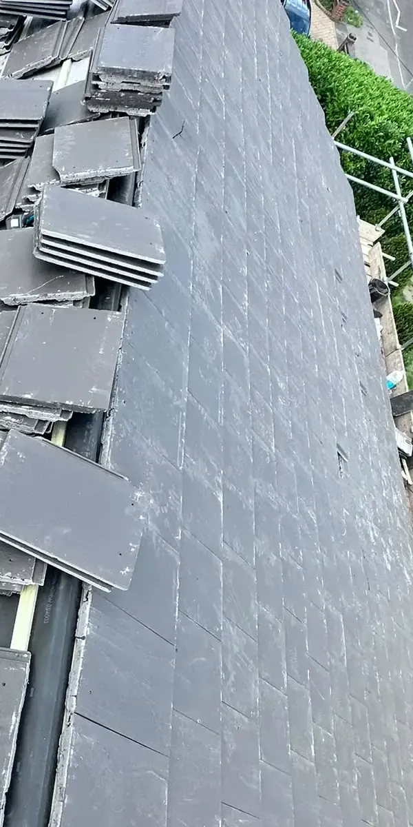 Grey roof tiles staged over visible membrane and battens beside installed courses in Weybridge
