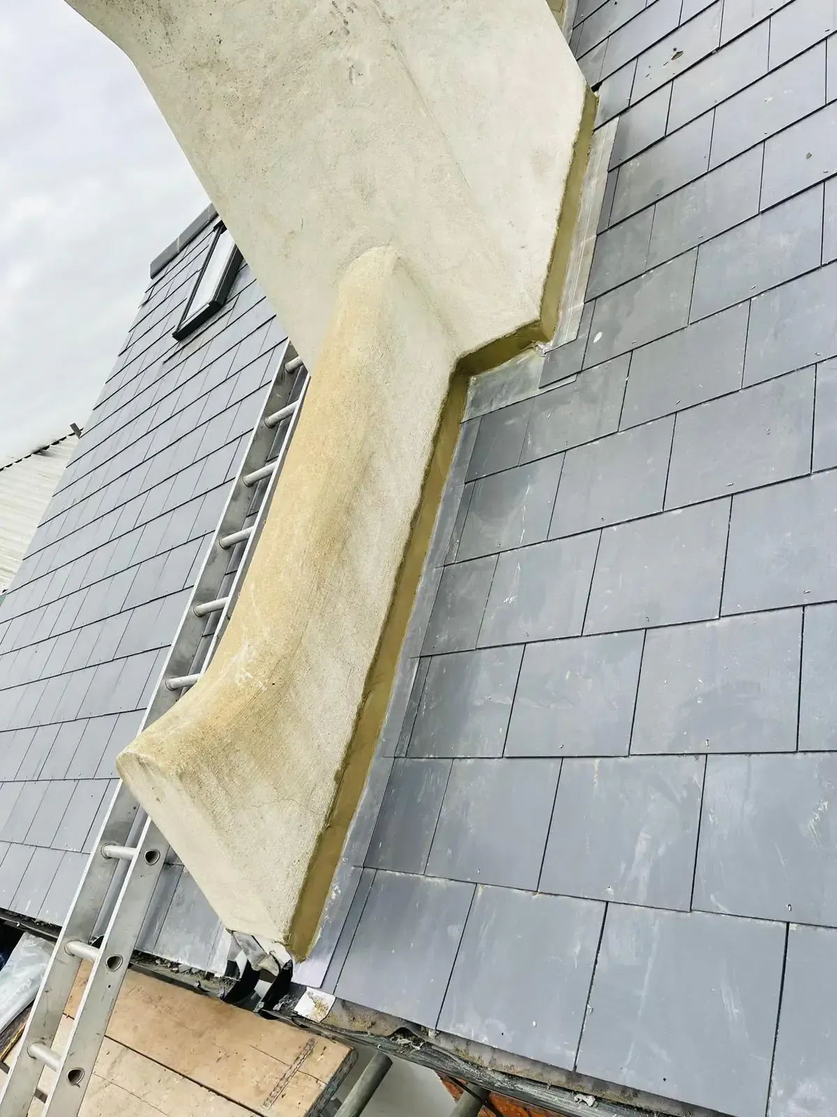 Slate-format roof slope and flashing beside a rendered chimney or abutment in Woking