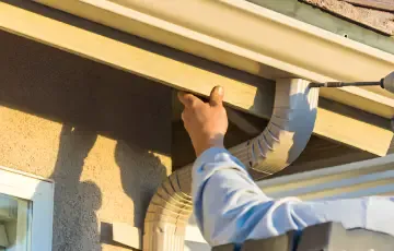 A hand positioning a dark gutter beneath roof eaves